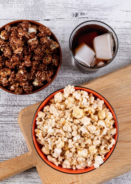 Vista superiore di popcorn in ciotole sul tagliere e limonata sul verticale di legno bianco