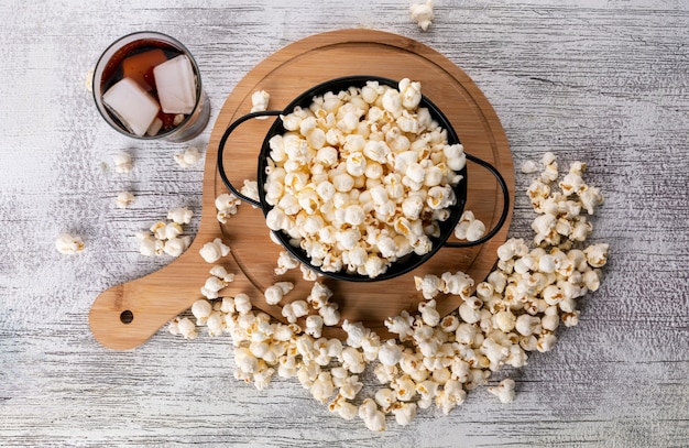 Vista superiore di popcorn in pentola nera e tagliere di legno con limonata sull'orizzontale di superficie di bianco