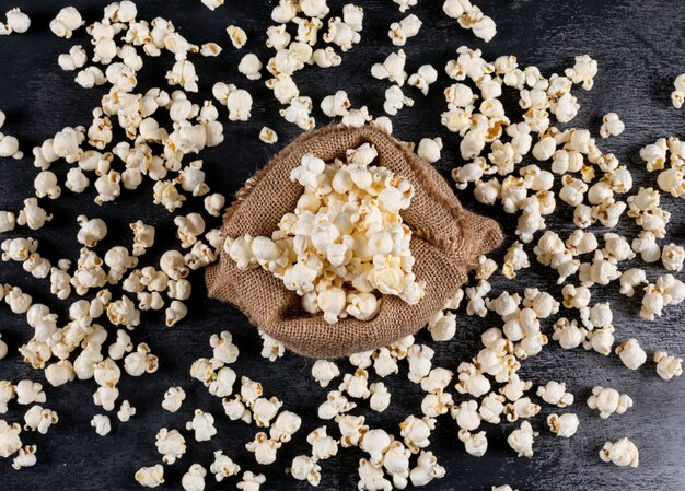 Vista superiore di popcorn nella borsa della tela di sacco sull'orizzontale nero