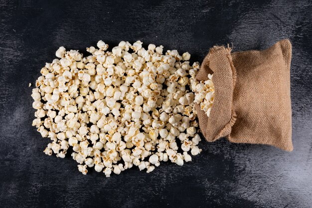Vista superiore di popcorn nella borsa della tela di sacco sull'orizzontale nero