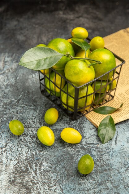 Vista verticale del cesto nero con mandarini verdi freschi e kumquat sui giornali su sfondo grigio