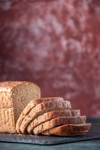 Vista verticale del coltello per fette di pane nero su tavola di colore scuro su sfondo marrone in difficoltà