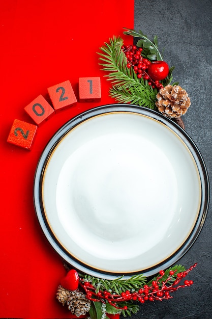 Vista verticale del fondo del nuovo anno con i rami e i numeri dell'abete degli accessori della decorazione del piatto di cena su un tovagliolo rosso su una tavola nera