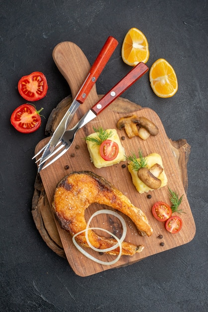 Vista verticale del gustoso pesce fritto e funghi pomodori verdi sul tagliere posate impostare pepe sulla superficie nera