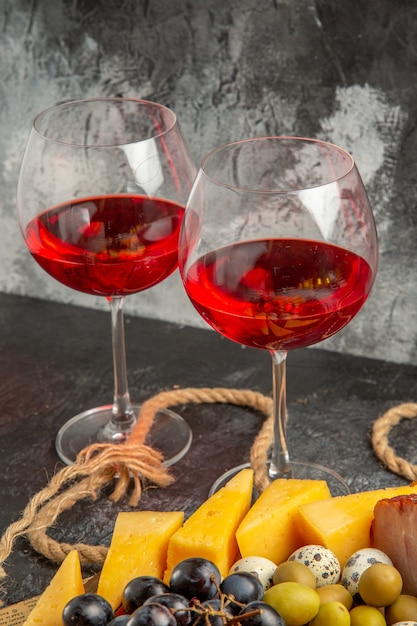 Vista verticale del miglior spuntino con vari frutti e cibi su un vassoio in legno marrone corda e due bicchieri di vino rosso su un vecchio giornale
