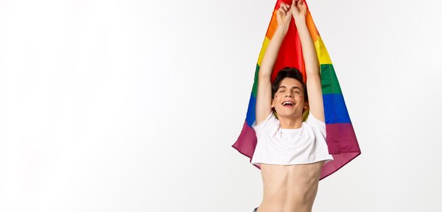 Vista verticale dell'uomo gay orgoglioso e felice che alza la bandiera arcobaleno lgbtq che sorride con emozione sollevata noi