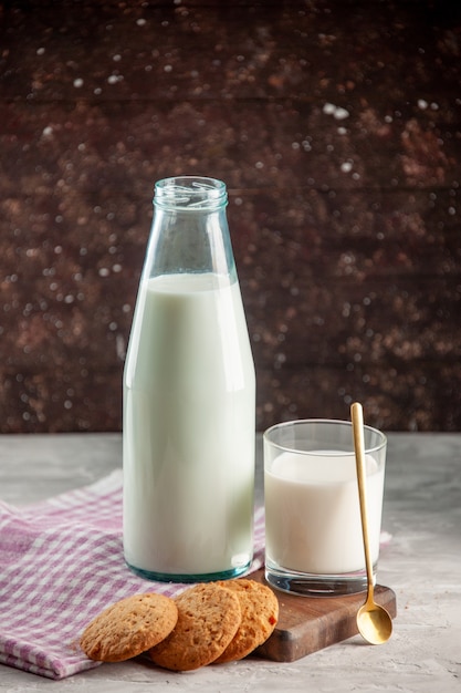 Vista verticale della bottiglia di vetro aperta e della tazza riempita di biscotti al latte su un asciugamano spogliato viola su un tagliere di legno