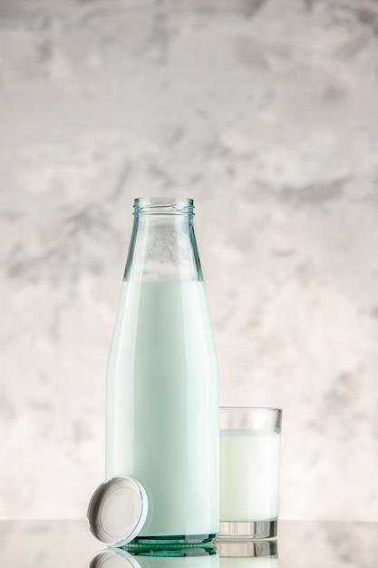 Vista verticale della bottiglia di vetro e della tazza riempita con tappo per il latte su sfondo bianco di fumo con spazio libero