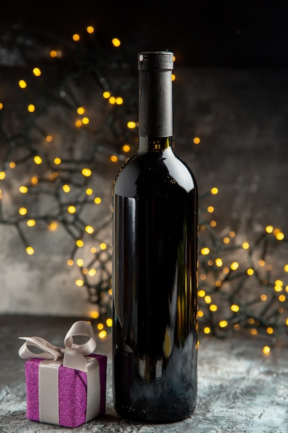 Vista verticale della bottiglia di vino rosso e del regalo di colore viola su sfondo grigio