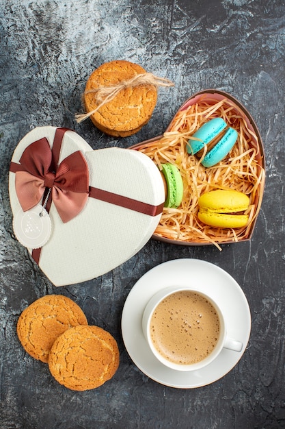 Vista verticale della confezione regalo con macarons e biscotti una tazza di caffè su sfondo scuro ghiacciato