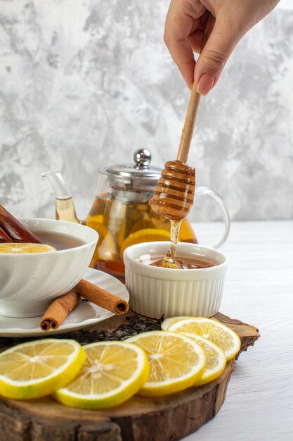 Vista verticale della mano che tiene il cucchiaio con tè nero al miele in una tazza bianca sul tavolo bianco