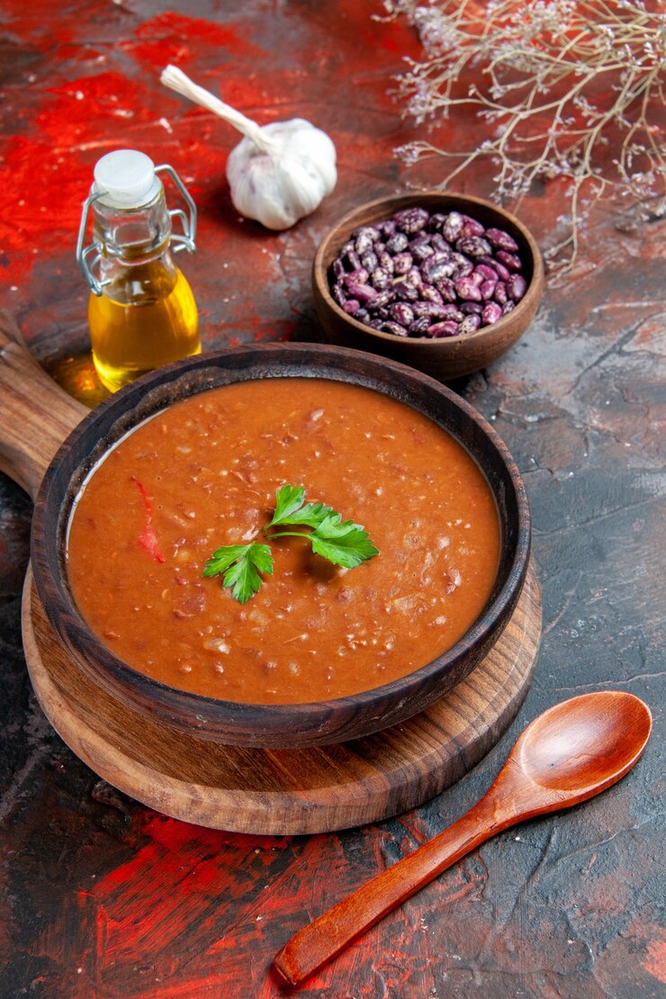 Foto gratuito vista verticale della zuppa di pomodoro su un tagliere marrone e fagioli su una tavola di colori misti