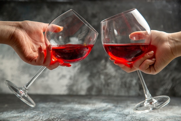 Vista verticale delle mani che tengono bicchieri di vino rosso secco su sfondo grigio