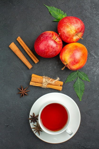 Vista verticale delle mele rosse organiche naturali fresche con i lime della cannella delle foglie verdi e una tazza di tè su fondo nero