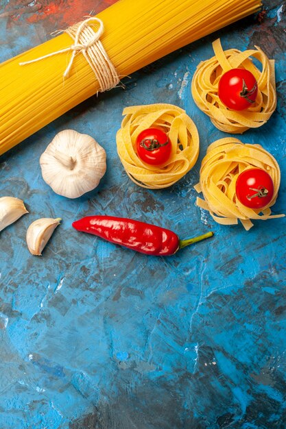 Vista verticale delle tagliatelle dei vermicelli legate con le corde e l'aglio dei peperoni su fondo blu