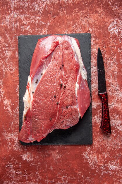 Vista verticale di carne rossa fresca cruda su tavola nera e coltello su fondo rosso pastello a olio con spazio libero