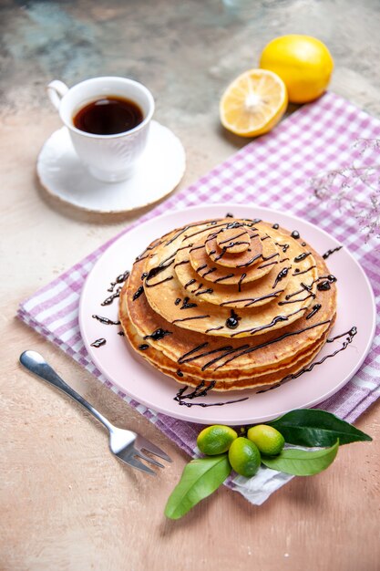 Vista verticale di deliziose frittelle classiche decorate con syrop al cioccolato su asciugamano spogliato rosa