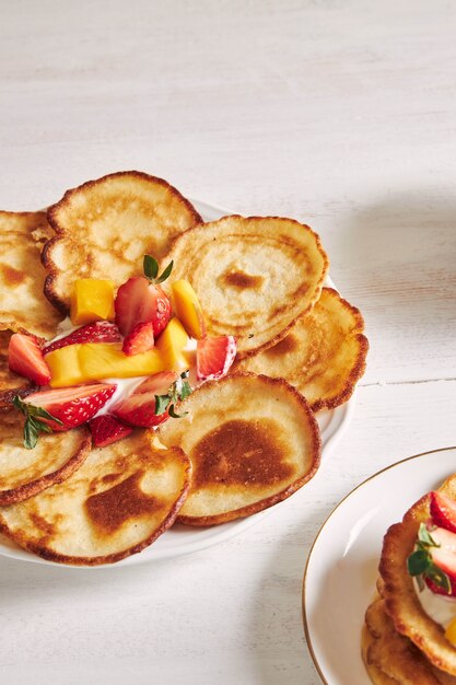 Vista verticale di deliziose frittelle con frutta su un tavolo di legno bianco