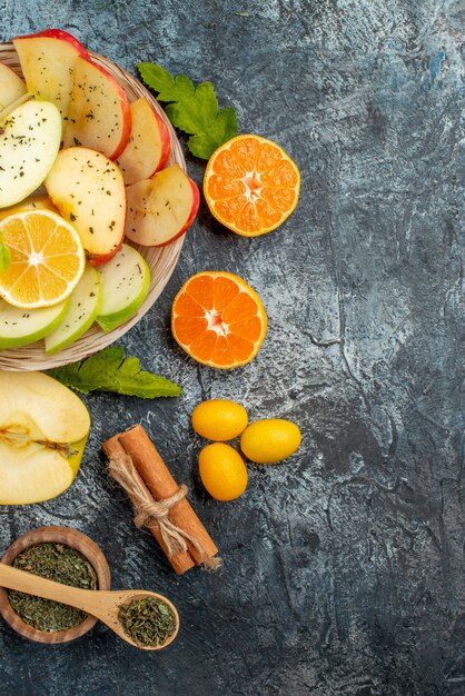 Vista verticale di fette di mela naturali fresche su un piatto bianco con limone e cannella lime kumquat arance su sfondo scuro