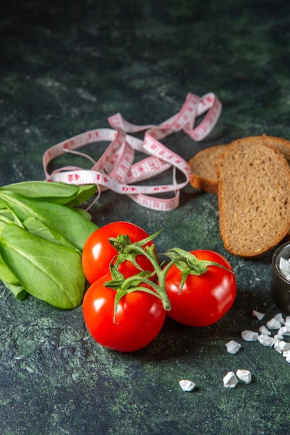 Vista verticale di fette di pane nero pomodori freschi con gambo e metri di sale fascio verde sulla superficie di colori scuri