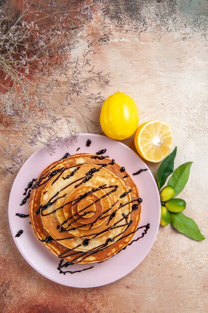 Vista verticale di frittelle soffocanti decorate con sciroppo di cioccolato e limone sul tavolo colorato