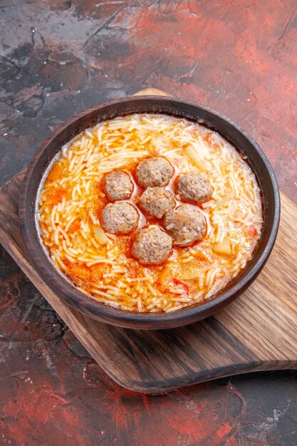 Vista verticale di gustosa zuppa di polpette con tagliatelle su tagliere di legno su sfondo scuro