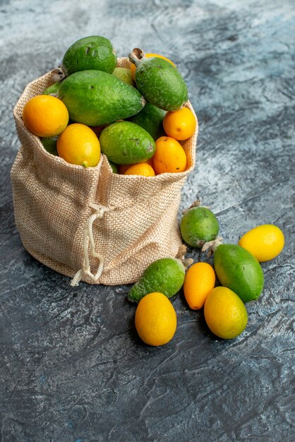 Vista verticale di kumquat freschi all'interno e all'esterno di una piccola borsa bianca su sfondo grigio