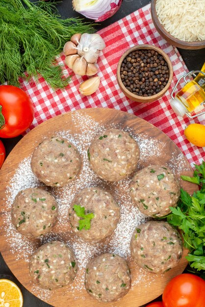 Vista verticale di polpette di carne cruda con verde in un piatto marrone e verdure fresche pepe di riso olio caduto bottiglia su asciugamano rosso su sfondo nero