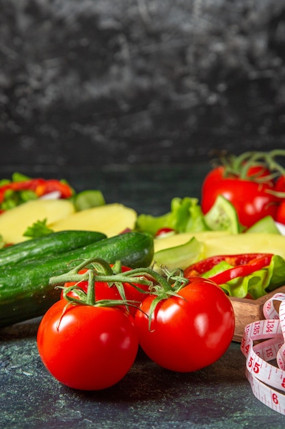 Vista verticale di pomodori freschi di verdure tritate con misuratore di stelo e cetrioli su un vassoio di legno sulla superficie di colori della miscela