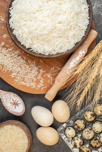 Vista verticale di riso lungo perfetto in pentole marroni e uova su tavola di legno su sfondo grigio