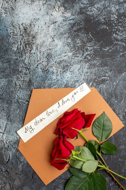 Vista verticale di rose rosse e busta con lettera d'amore su sfondo scuro ghiacciato