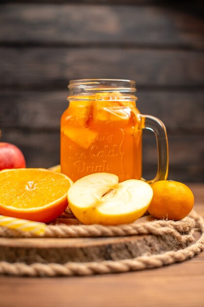 Vista verticale di succo fresco biologico in una bottiglia servita con tubo e frutta su un tagliere e su un tavolo di legno marrone