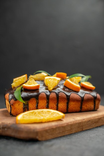 Vista verticale di torte morbide sul tagliere e limoni tagliati con foglie su sfondo scuro