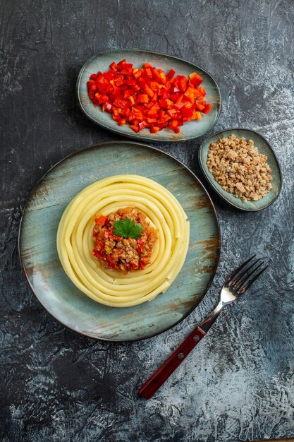 Vista verticale di un delizioso pasto di pasta su un piatto blu servito con pomodoro e carne per cena e forchetta
