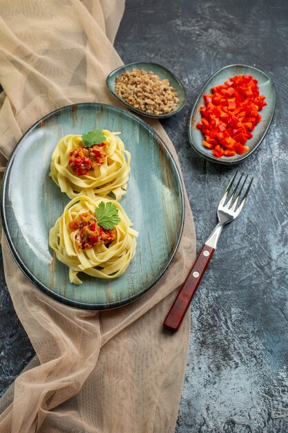 Vista verticale di un delizioso pasto di pasta su un piatto blu servito con pomodoro e carne per cena su un asciugamano color marrone chiaro i suoi ingredienti