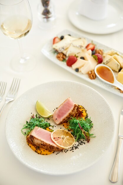 Vista verticale di un delizioso piatto di tonno con un bicchiere di vino e un set di formaggi