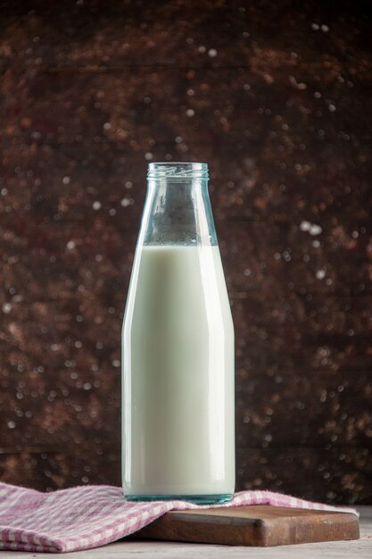 Vista verticale di una bottiglia di vetro aperta riempita di latte su un asciugamano spogliato viola su un tagliere di legno