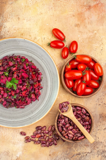 Vista verticale di una deliziosa insalata con barbabietola rossa e fagioli e fagioli dentro e fuori la pentola e i pomodori su un tavolo a colori misti