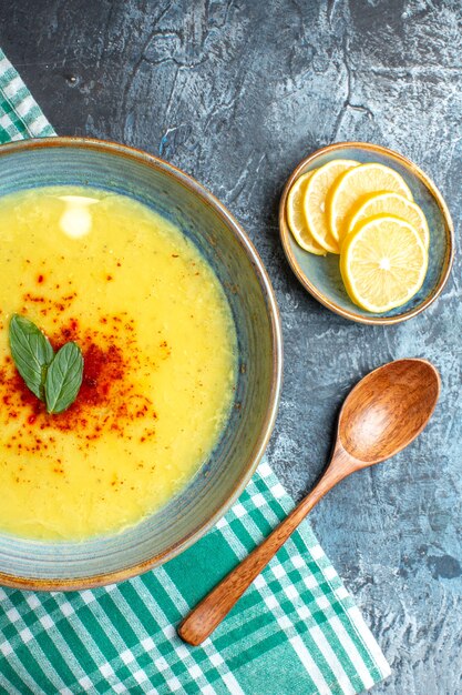 Vista verticale di una pentola blu con zuppa gustosa servita con menta e pepe accanto al cucchiaio di legno di limone tritato su sfondo blu