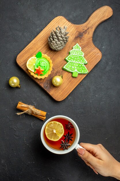 Vista verticale di una tazza di tè nero xsmas accessori cono di conifere e lime alla cannella su un tagliere di legno su sfondo nero