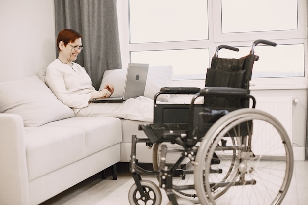 Vita delle persone disabili. La donna matura giaceva sul divano con il computer portatile.