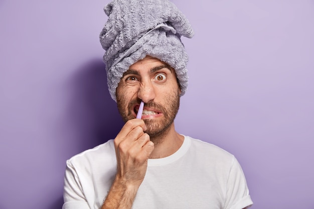 Vita quotidiana e concetto di coccole. Close up ritratto di giovane uomo coglie i capelli dalla narice con una pinzetta, soffre di dolore