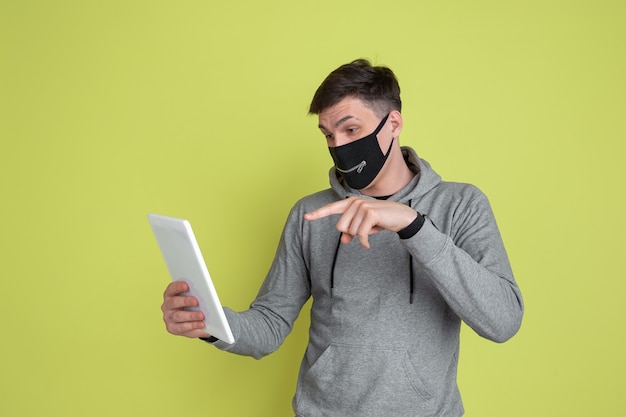 Vlog, selfie. Il ritratto dell'uomo caucasico isolato sulla parete gialla dello studio. modello maschile in maschera facciale nera.