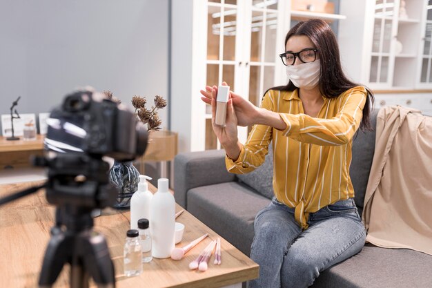 Vlogger femminile a casa con fotocamera e maschera facciale