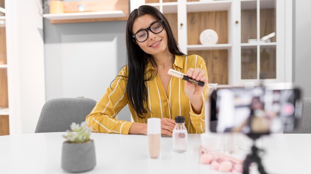 Vlogger femminile a casa con smartphone e prodotti per il trucco