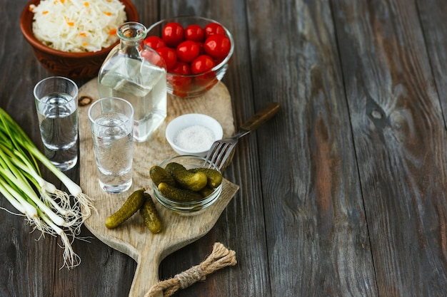 Vodka con verdure salate su superficie di legno. Bevanda alcolica artigianale pura e snack tradizionale, pomodori, cavoli, cetrioli. Spazio negativo. Celebrando il cibo e delizioso.