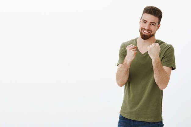 Voglio combattere, vieni e prendilo. Ritratto di uomo barbuto bello felice bello eccitato e giocoso con gli occhi azzurri che tengono i pugni come pugile pronto a pugni, sorridente sopra il muro bianco