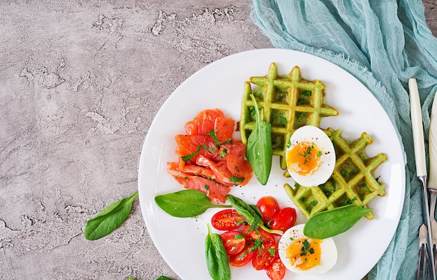 Waffle salati con spinaci e uovo, pomodoro, salmone in zolla bianca. Cibo gustoso. Vista dall'alto. Disteso