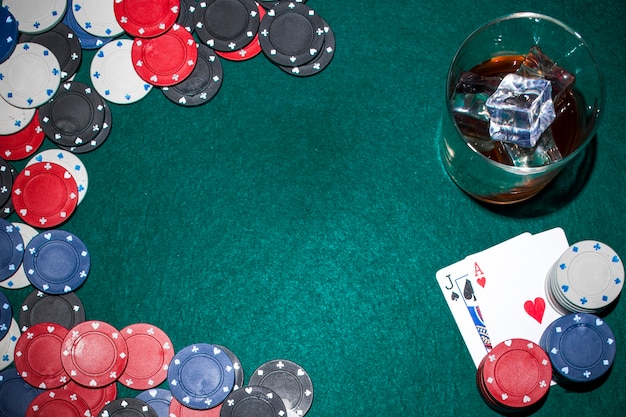 Whisky con cubetti di ghiaccio e fiches del casinò e carta da gioco sul tavolo da poker verde