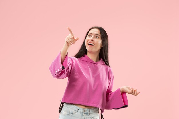 Wow. Bello ritratto anteriore mezzo busto femminile isolato sul backgroud rosa dello studio. Giovane donna sorpresa emotiva in piedi con la bocca aperta. Emozioni umane, concetto di espressione facciale. Colori alla moda